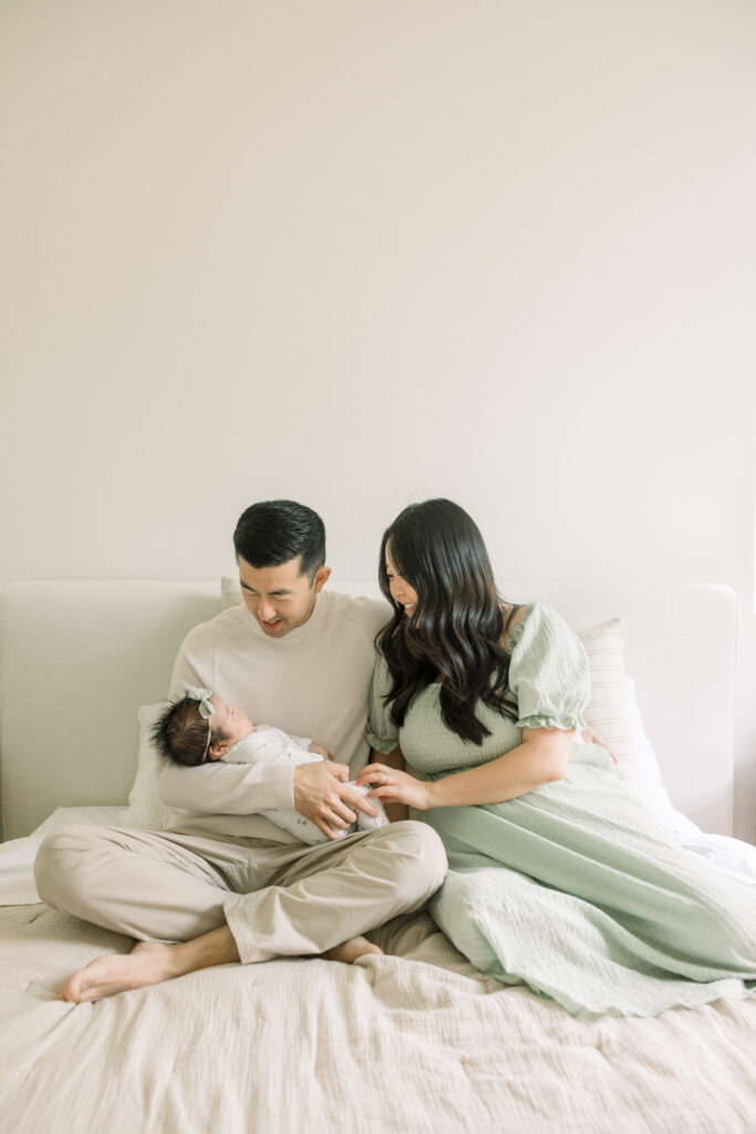 mom and dad with baby sitting on bed